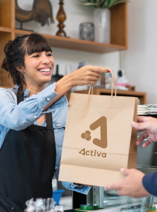 Mujer sonriente entregando una bolsa de papel personalizada con logo impreso en un negocio. Packaging ecológico y sostenible.